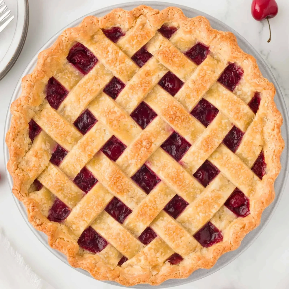 Rhukra Cake House almond tart with a golden lattice crust and visible red cherry fruit filling on a white surface.