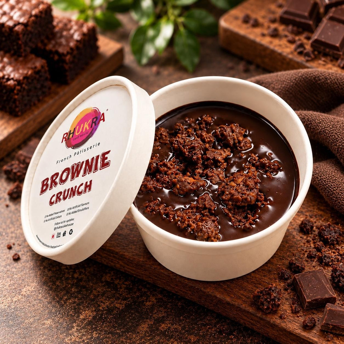 Rhukra Cake House Brownie Crunchy dessert in a white paper cup with chocolate chunks on a rustic wooden board.