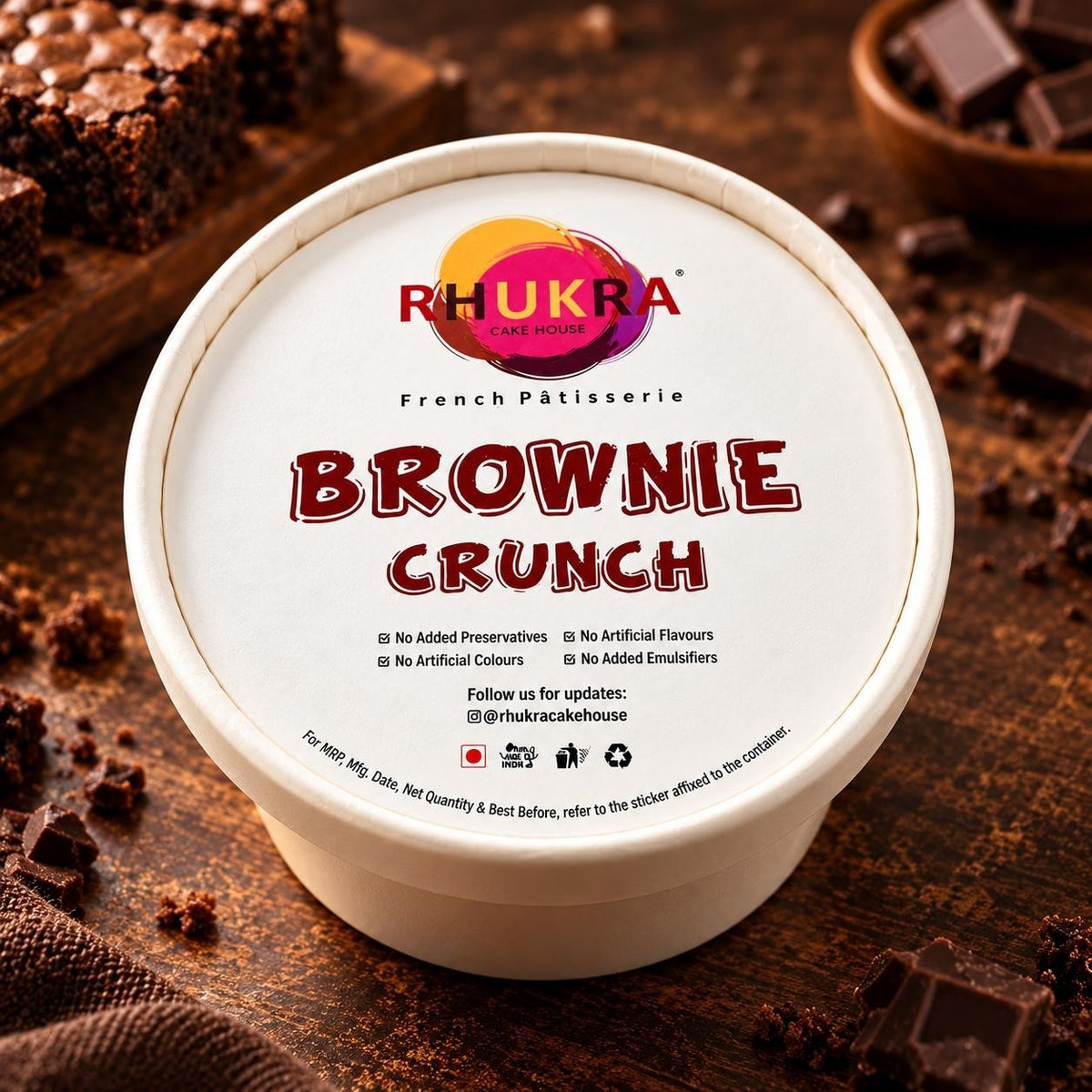 Rhukra Cake House Brownie Crunchy dessert in a white paper tub on a wooden table with chocolate chunks