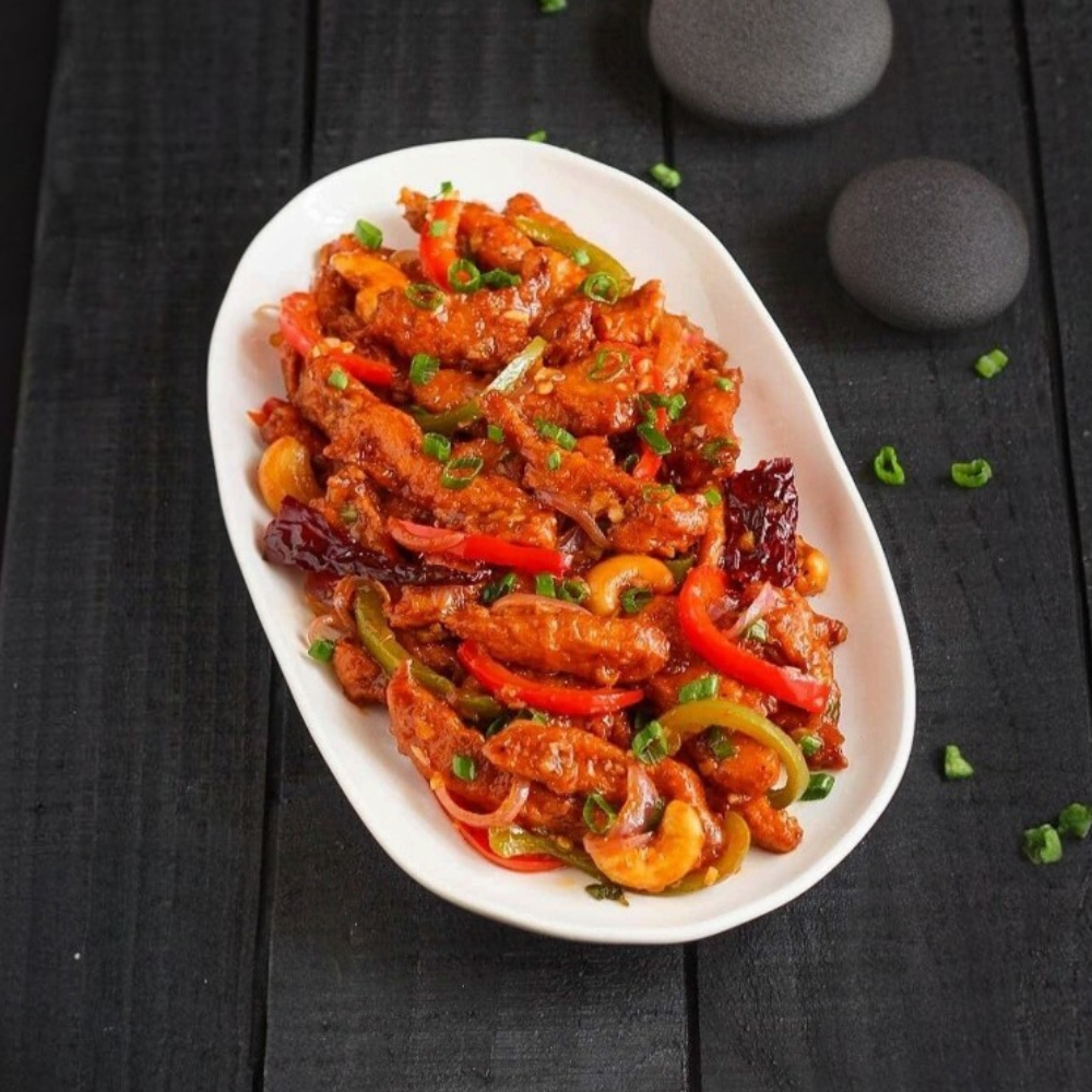 Rhukra Cake House Dragon Chicken stir-fry with cashews, bell peppers, and onions served on a white oval plate
