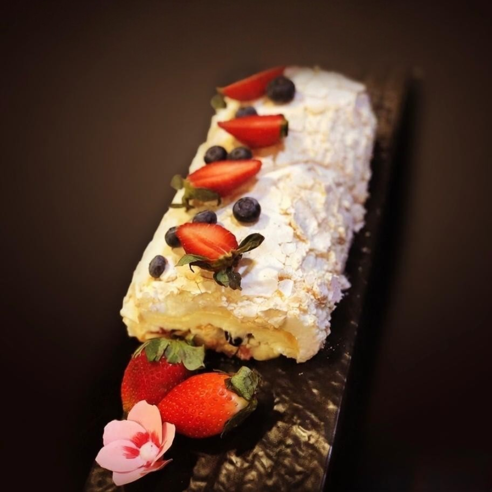 Rhukra Cake House Fruity Meringue roll topped with fresh strawberries and blueberries on a dark serving platter